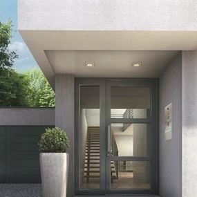 Moderne Hauseingangstür aus Glas und Aluminium mit Treppenhaus und Pflanzkübel.